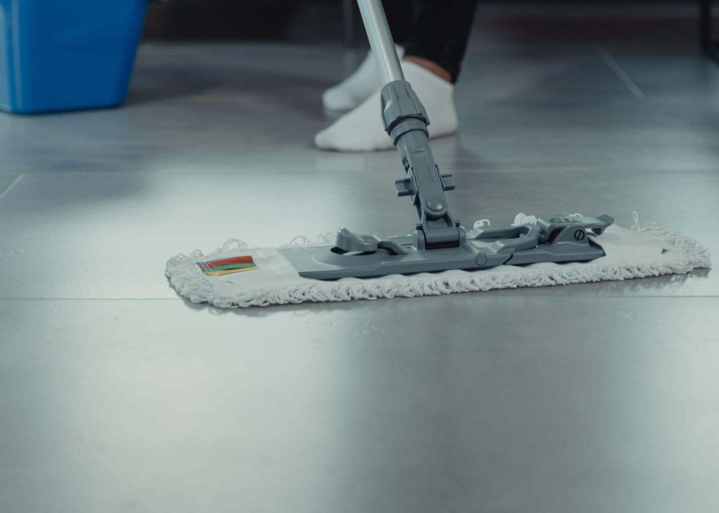 Close-up of a flat mop head sweeping a light tiled floor, leaving a clean streak behind